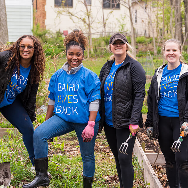 Four Baird associates wearing Baird Cares t-shirts while standing in a community garden.