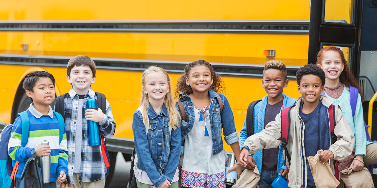 Group of elementary school children standing in front of a school bus