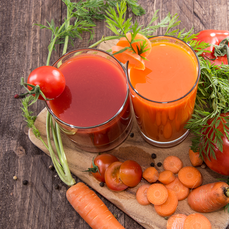 Two glasses of vegetable juice sitting on a wooden cutting board.