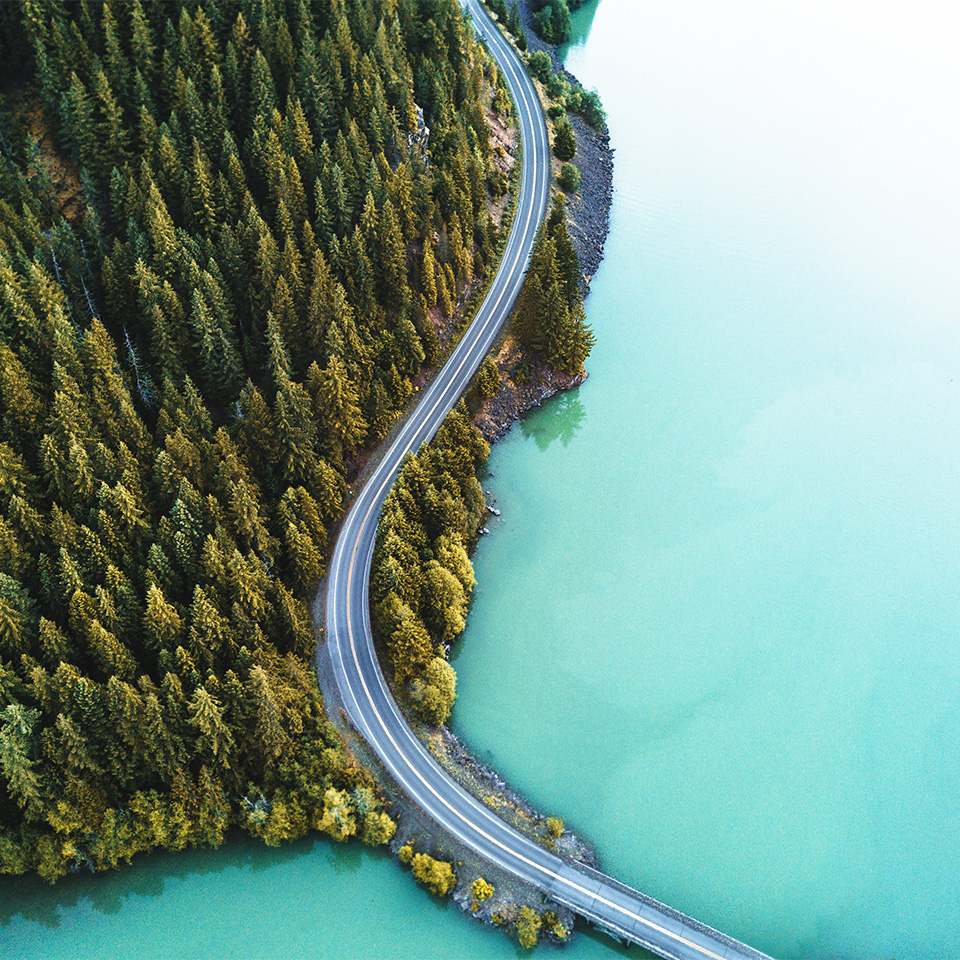 Aerial shot of a winding road along a wooded coastline