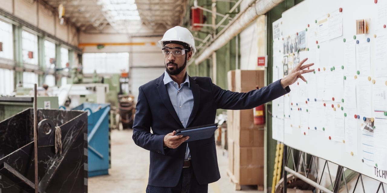 Project manager standing at whiteboard wearing hardhat