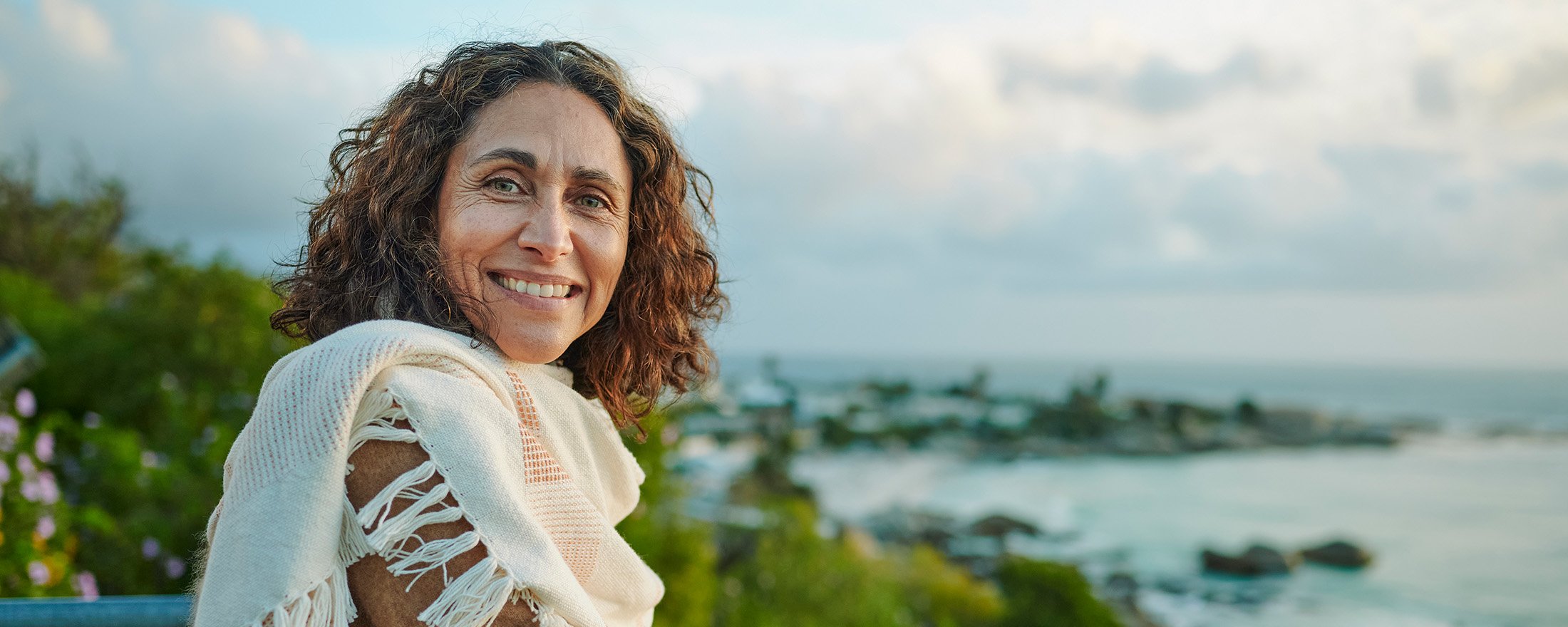 Woman standing on a pier overlooking a tree-lined coastline