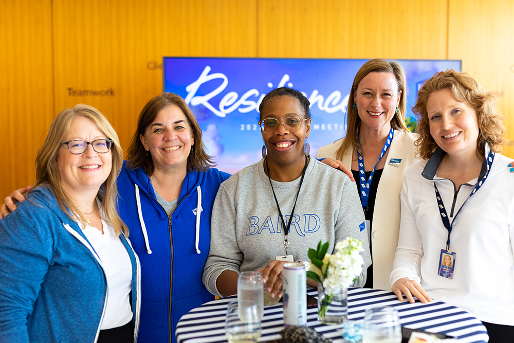 Group of five women standing together at a reception table wearing Baird branded clothing.