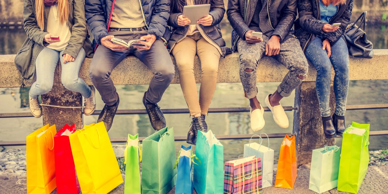 Group of people sitting in a line on a wall with shopping bags in front of them on the ground.