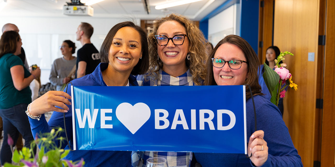 Three women holding a 'we love Baird' banner