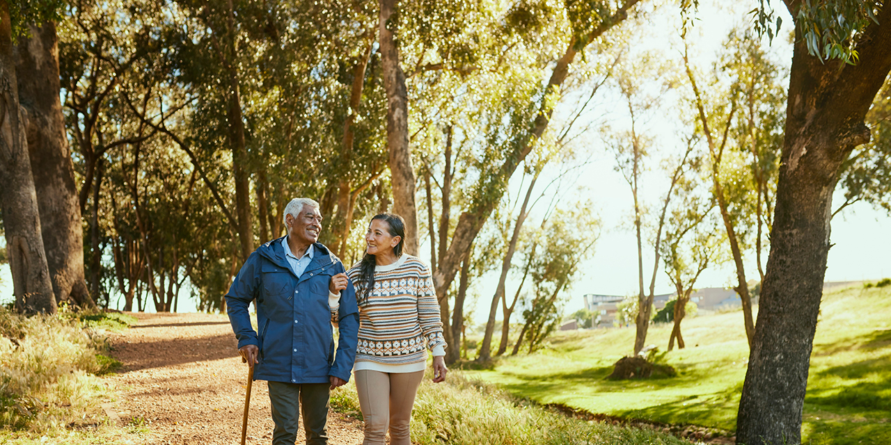 Elderly couple walking on a path in the woods.