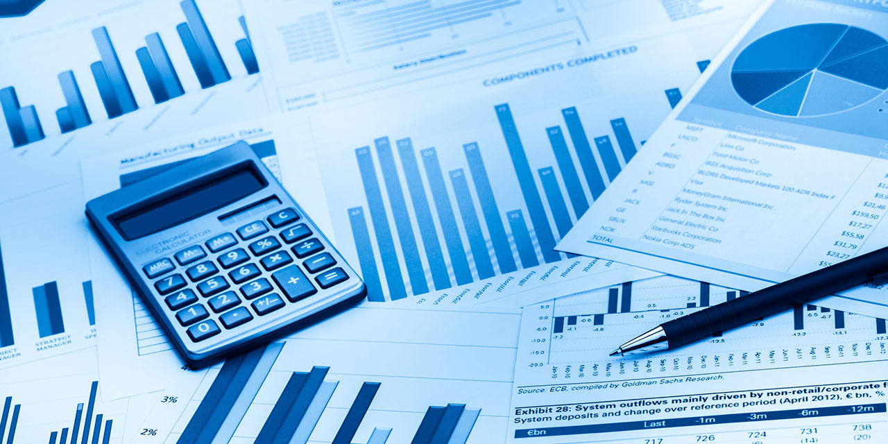 A calculator and pen lying on top of business documents showing pie charts and graphs.